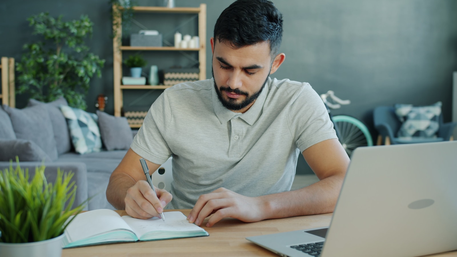 Person writing a focused plan beside a laptop